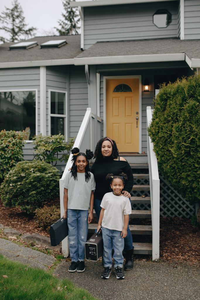 A joyful family standing together in front of their house with a yellow door, exuding warmth and happiness.